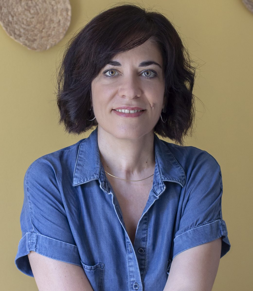 Η Ζωή Τριανταφυλλίδου, ψυχοθεραπεύτρια στις Διαδρομές, καθιστή με σταυρωμένα χέρια μπροστά σε κίτρινο φόντο